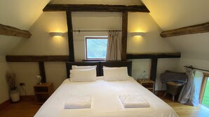 A bedroom with a large bed, two bedside tables, a window with curtains, and wooden beams on the ceiling.