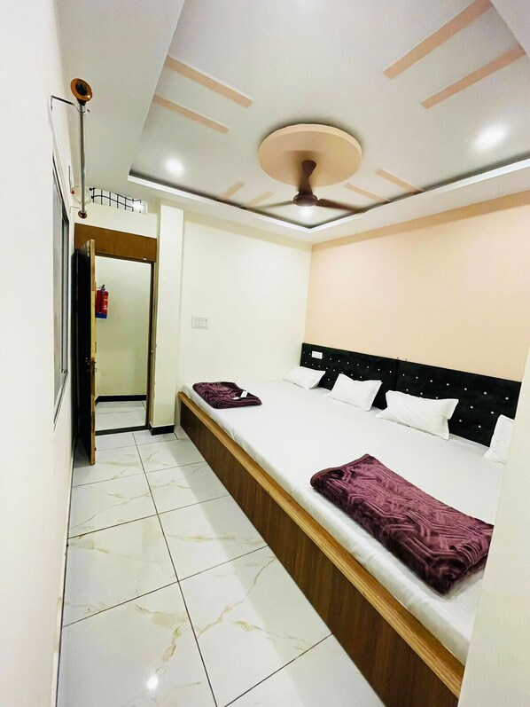 Une chambre d’hôtel avec un lit, un ventilateur de plafond et une porte donnant sur un couloir.