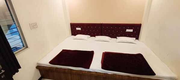 Una cama individual con cabecera de madera, ropa de cama blanca y dos almohadones rojos.