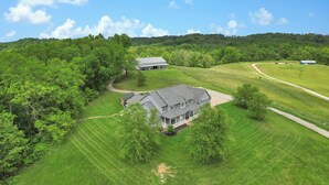 A large house surrounded by lush green fields and trees. - Spacious Getaway for 22 w/ Pool, Hot Tub & Huge Game Room – Perfect for Groups! (Logan)
