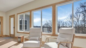 A room with two beige armchairs, a wooden floor, a large window with a view of trees, and a small wooden side table. - Spacious Getaway for 22 w/ Pool, Hot Tub & Huge Game Room – Perfect for Groups! (Logan)