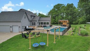 A residential property with a covered patio, a swimming pool, and a swing set. - Spacious Getaway for 22 w/ Pool, Hot Tub & Huge Game Room – Perfect for Groups! (Logan)