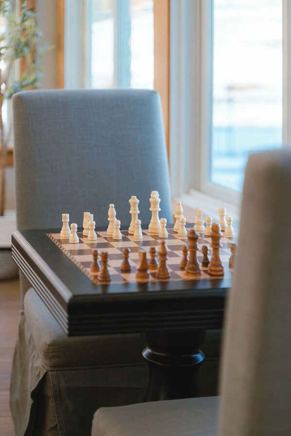 Un échiquier posé sur une table dans une pièce dotée d’une grande fenêtre et d’une chaise bleue.
