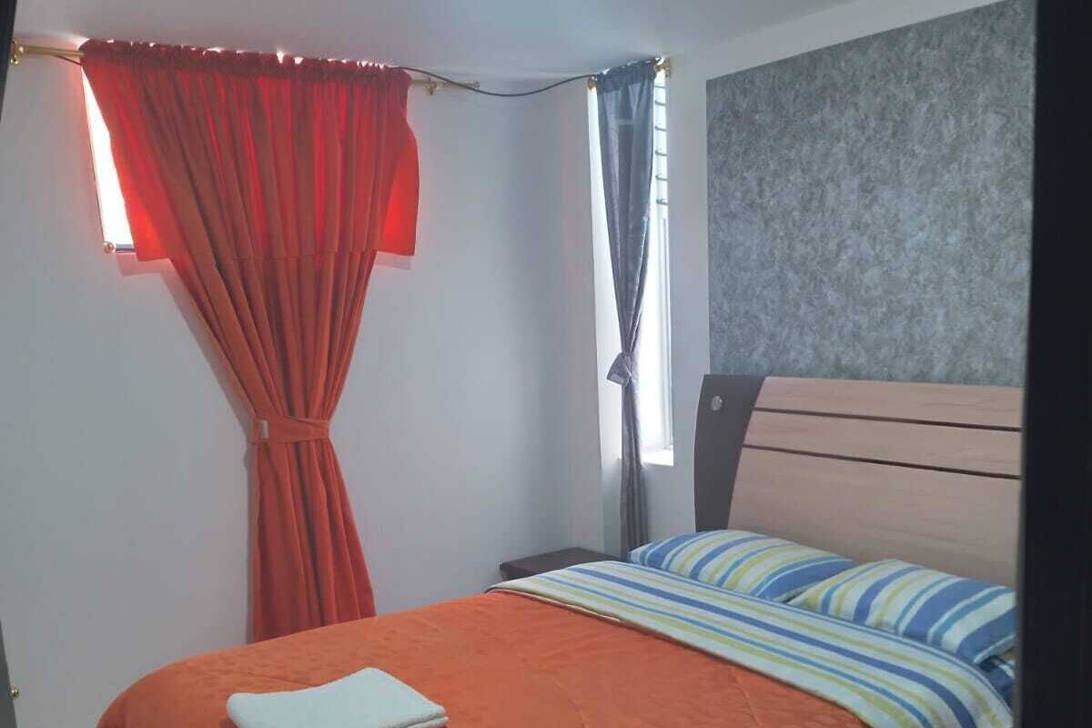 A bedroom with a bed, a window with curtains, a headboard, and a ceiling light.