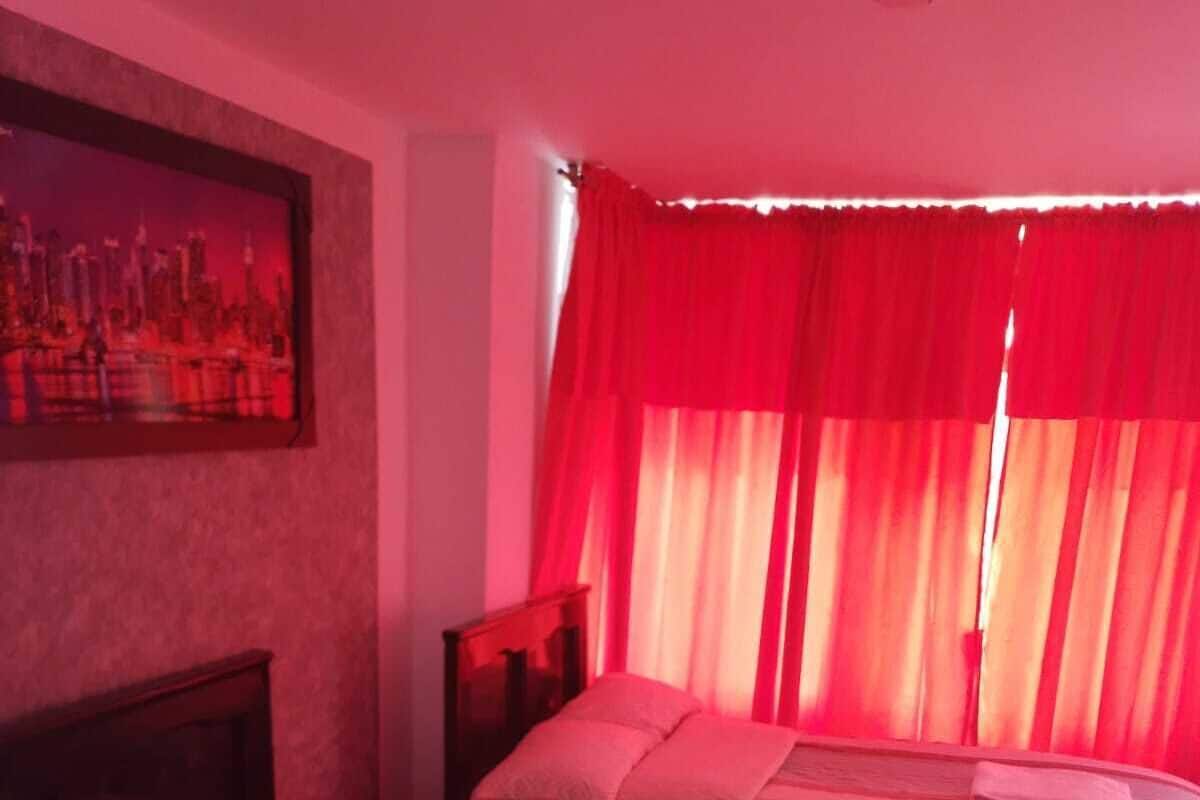 A hotel room with two beds, a cityscape painting on the wall, and red curtains.