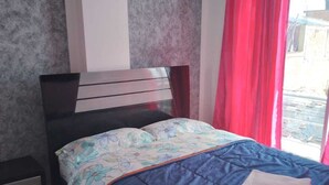 A bedroom with a bed, a nightstand, a window with red curtains, and a marble floor. - Hotel Paraiso Real (Cumbal)