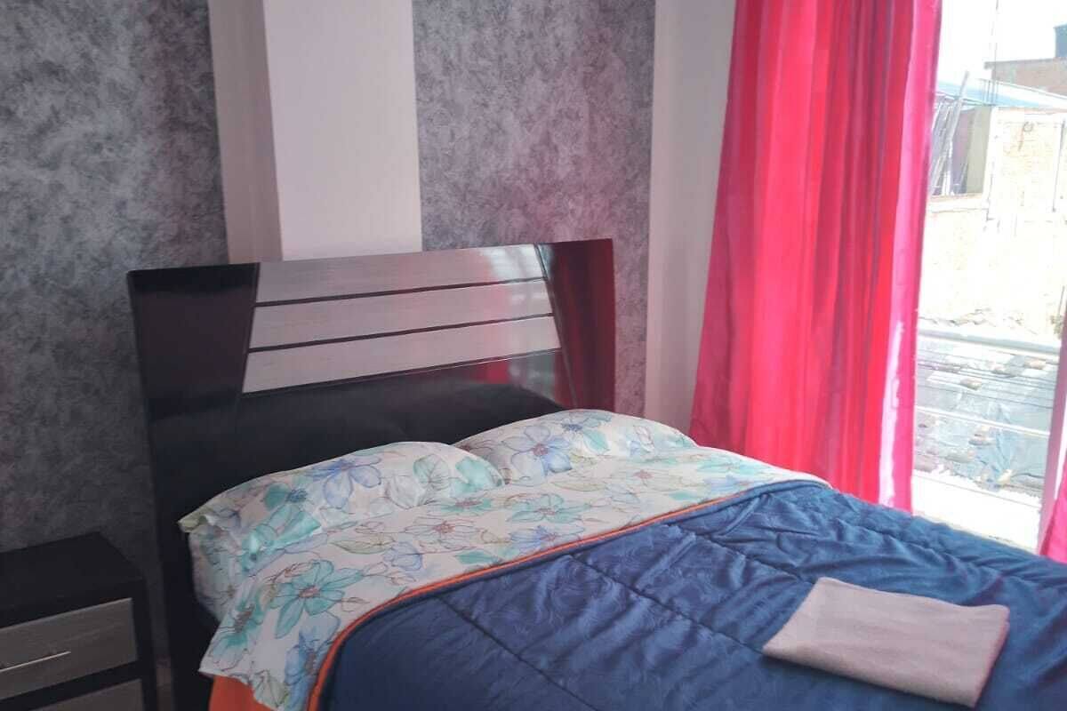 A bedroom with a bed, a nightstand, a window with red curtains, and a marble floor.