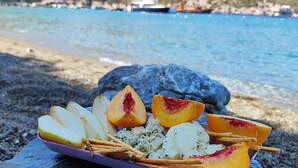 A stone table with a fruit platter on a rocky beach with boats in the background.