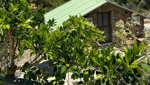 A stone building with a green roof, surrounded by lush greenery and overlooking a mountainous landscape with a clear blue sky.