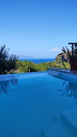 Ein klares, blaues Schwimmbecken mit Blick auf das Meer und die dahinterliegenden Berge.