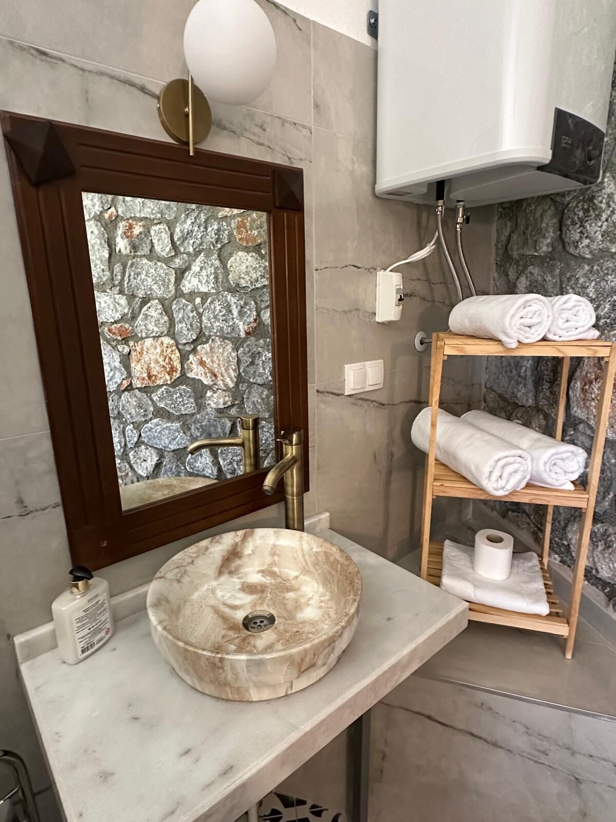 Un baño con pared de piedra, un estante de madera con toallas y un lavabo de mármol.