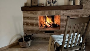 Een gezellige kamer met een metselwerk open haard, een houten stoel en een mand op de vloer.