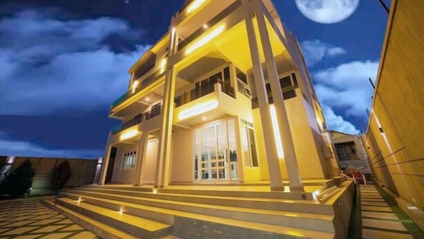 Un bâtiment moderne avec un escalier menant à l’entrée, sous un ciel nocturne où l’on peut voir la lune.