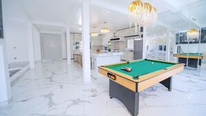 Un vaste espace intérieur doté d’une table de billard, d’un sol en marbre et de lustres modernes.