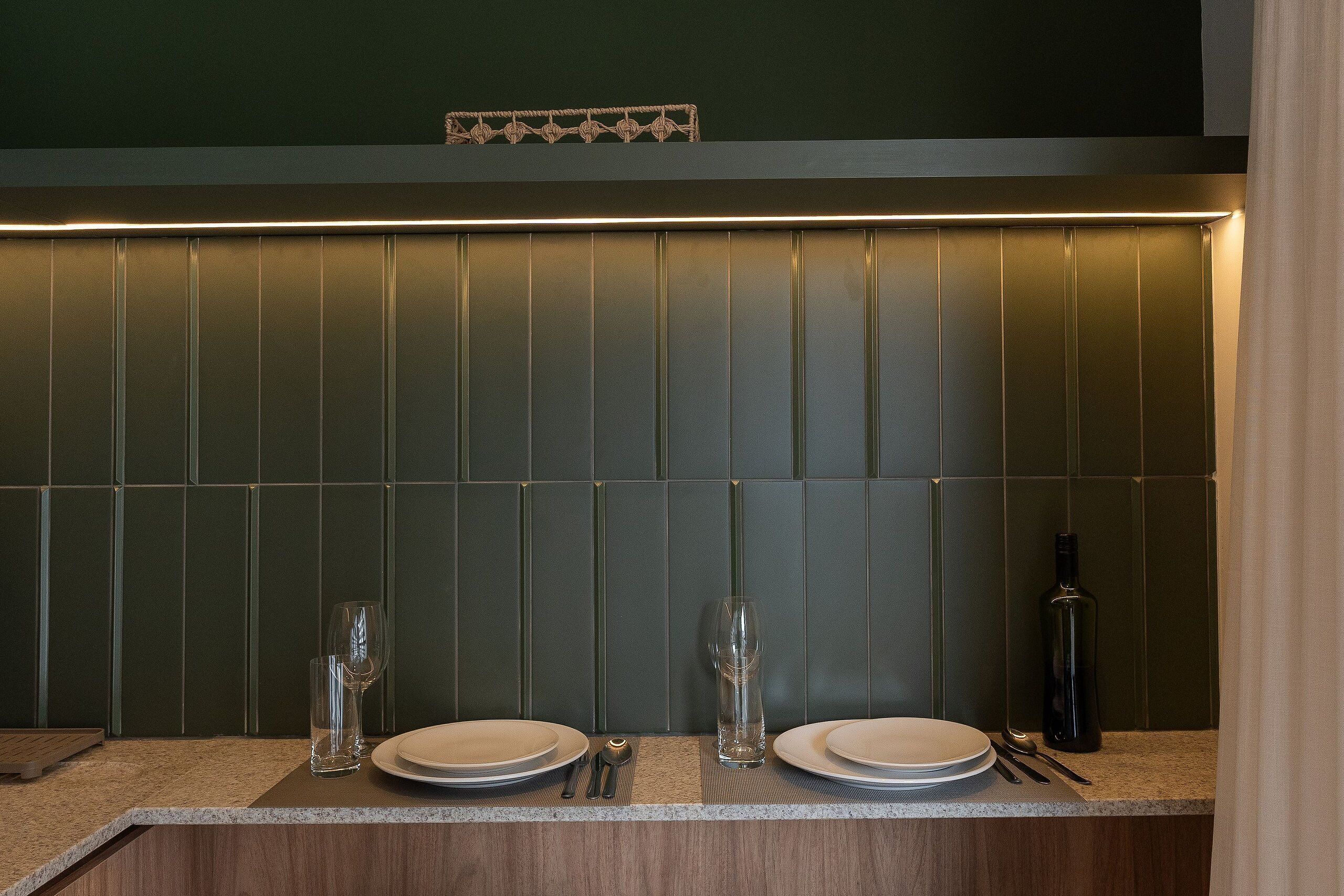 A neatly set dining table with plates, cutlery, and a wine bottle, against a green wall with vertical paneling.
