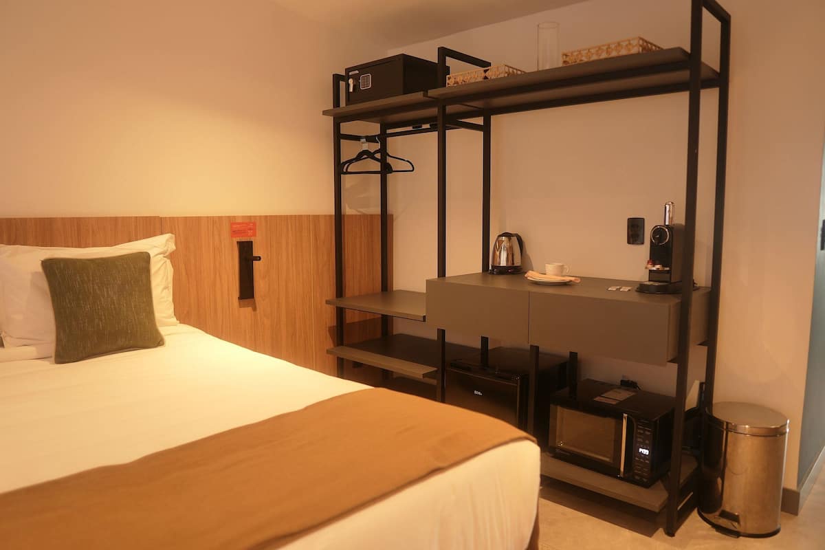 Ett hotellrum med en säng, ett skrivbord med en kaffebryggare, en mikrovågsugn och en papperskorg.