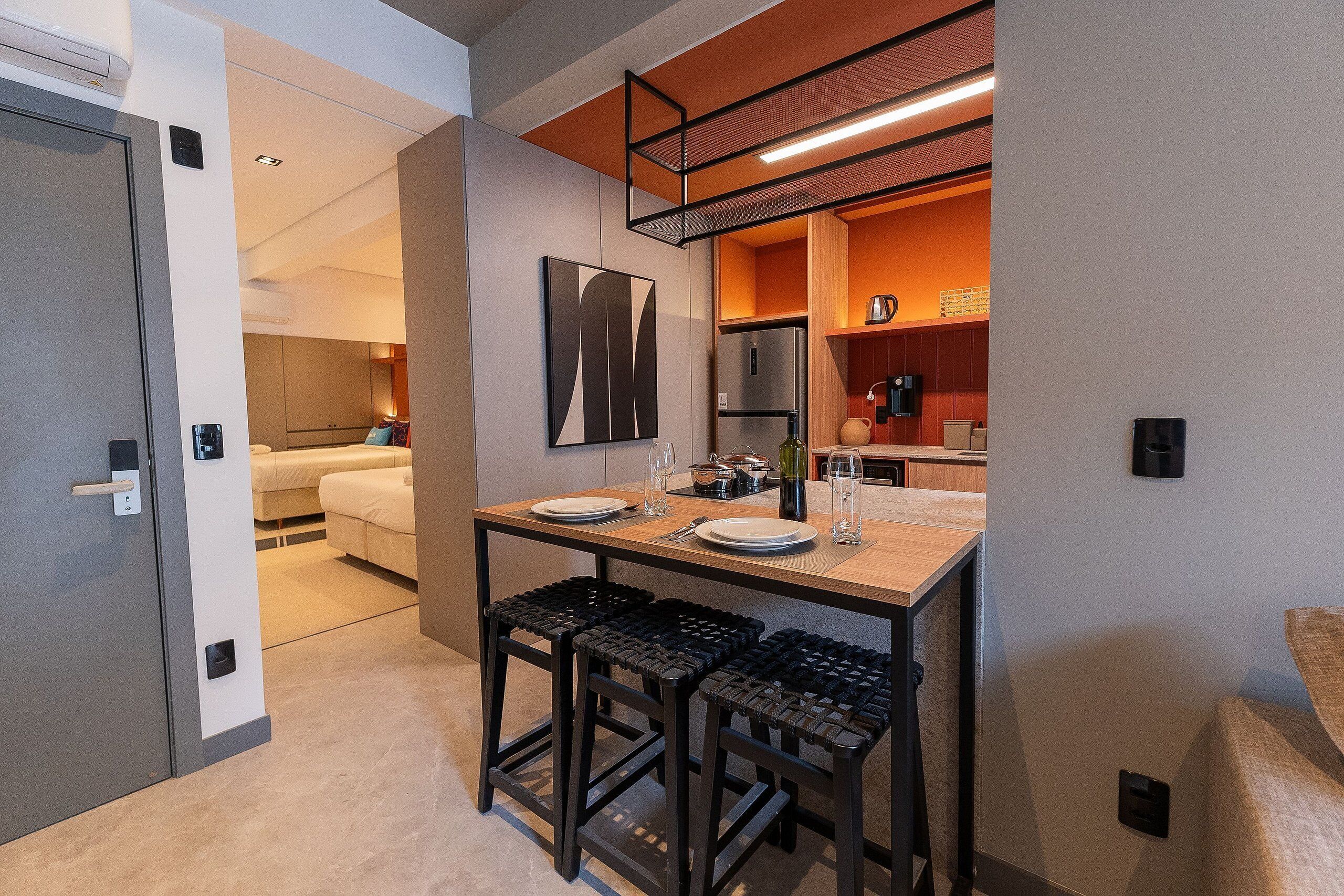 Habitación de hotel compacta con kitchenette, comedor con mesa y sillas, y una cama al fondo.