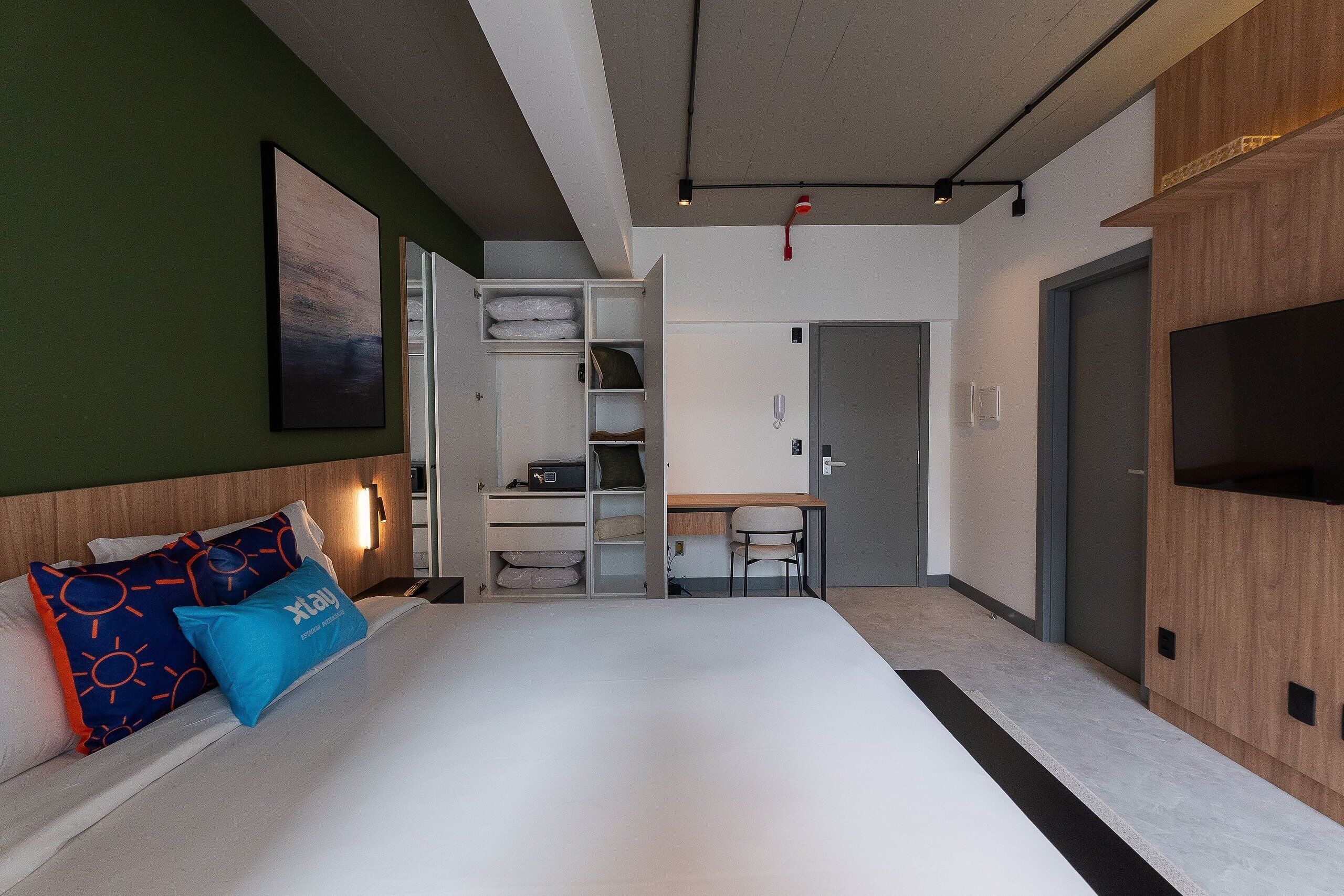 A modern hotel room with a large bed, a desk, and a wardrobe.