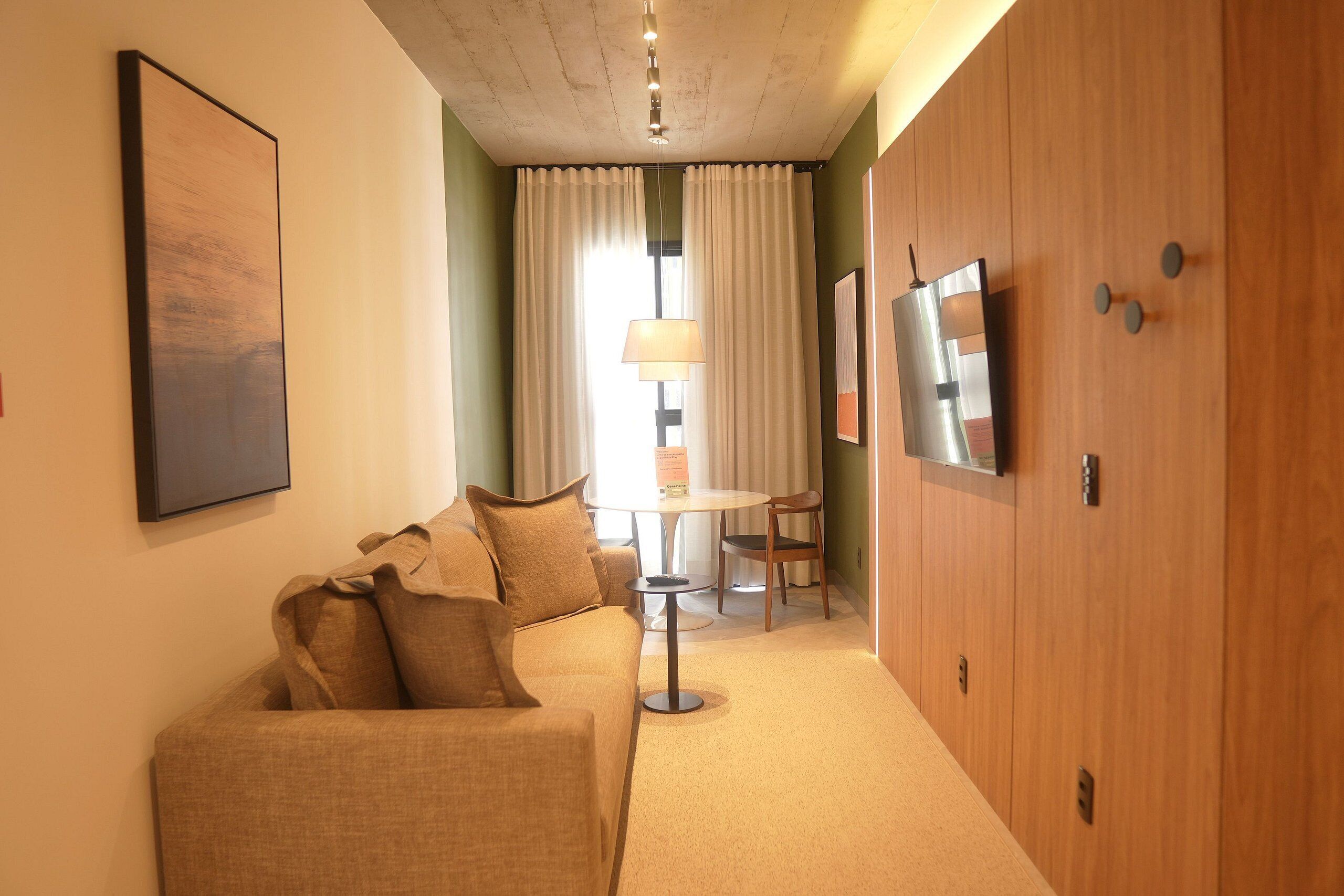 Una habitación de hotel con sofá, televisión, mesa con lámpara y cortinas.