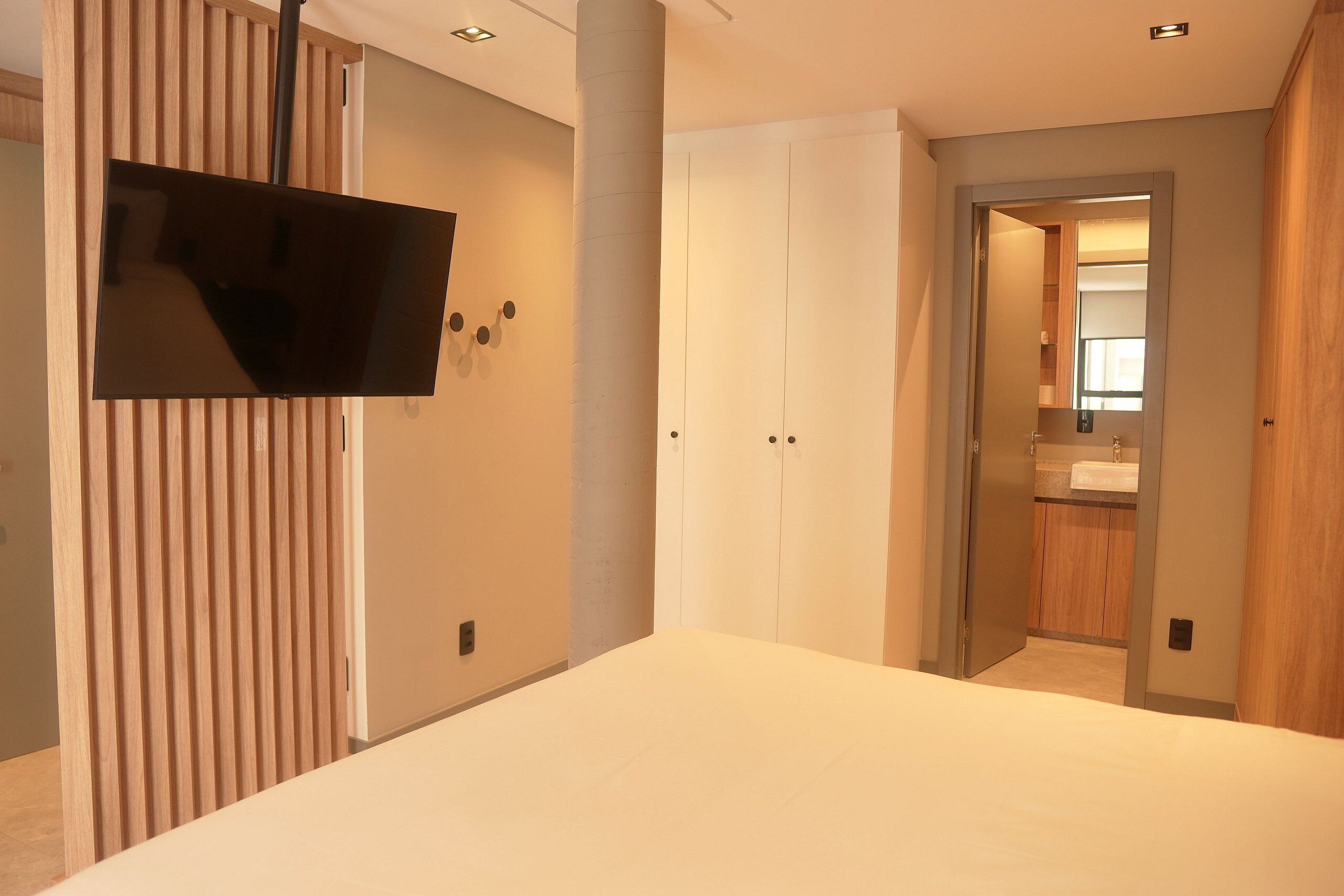 Une chambre moderne avec un grand lit, un téléviseur fixé au mur et un dressing.