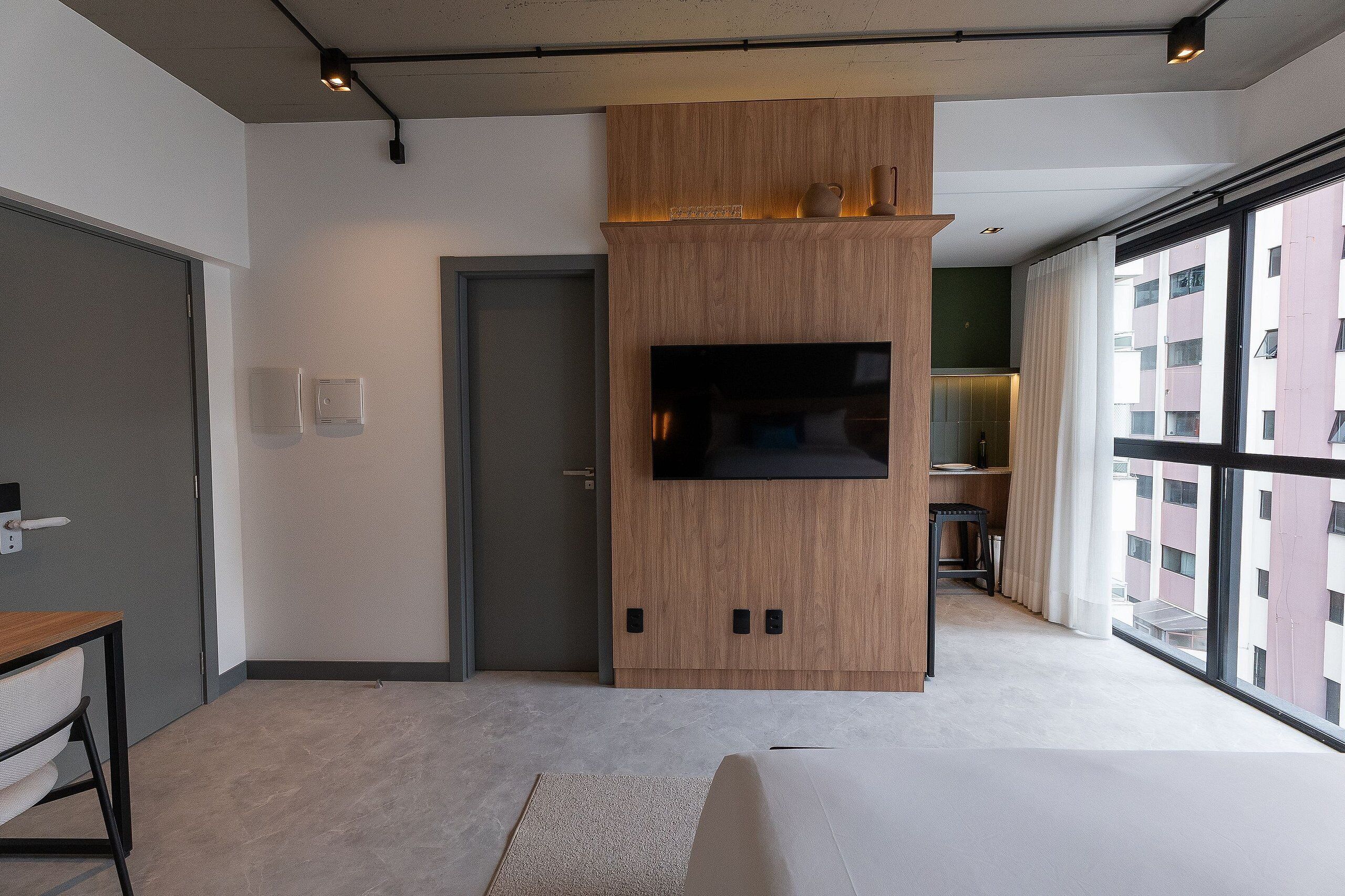A modern living room with a built-in TV, a wooden accent wall, a large window, and a door leading to another room.