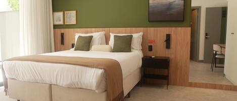 A bedroom with a large bed, a nightstand, an air conditioning unit, a painting, and a door leading to another room.