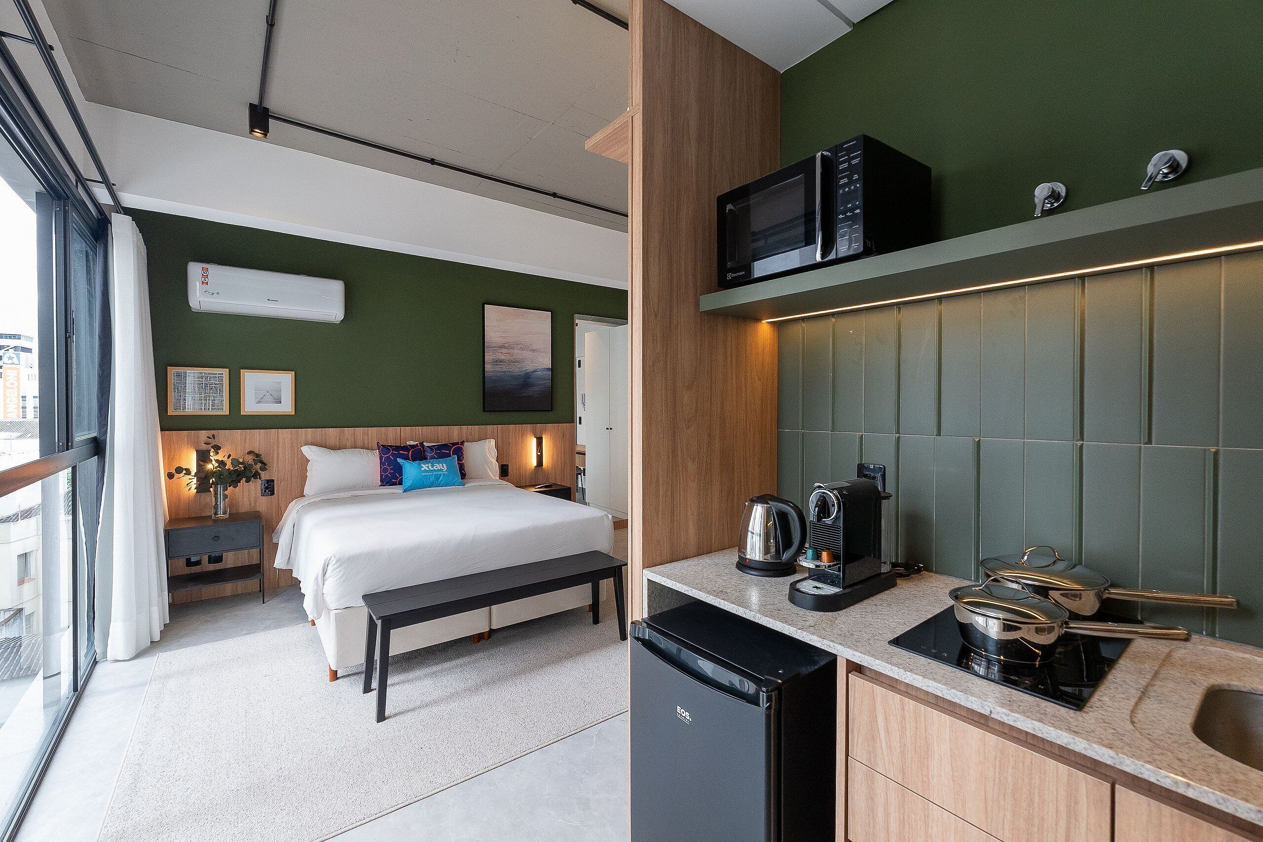 Ein modernes Hotelzimmer mit Bett, Nachttisch und einer Küchenzeile mit Mikrowelle und Wasserkocher.