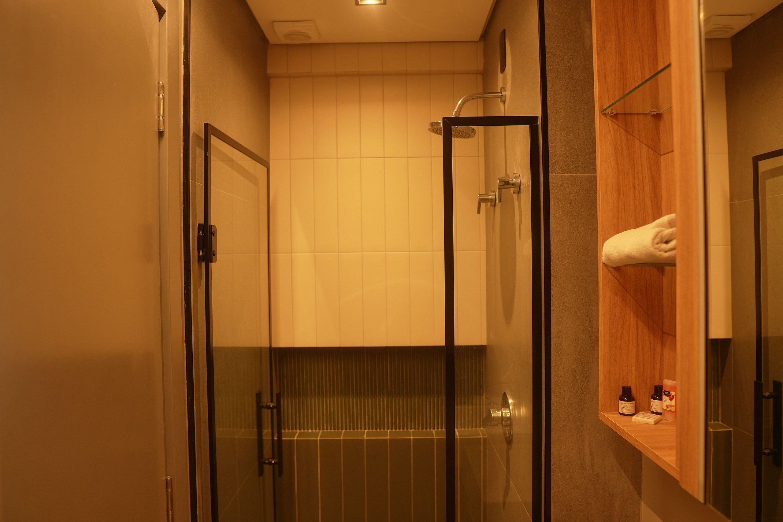 Une douche fermée par des parois en verre, avec un meuble-lavabo en bois et un porte-serviettes.