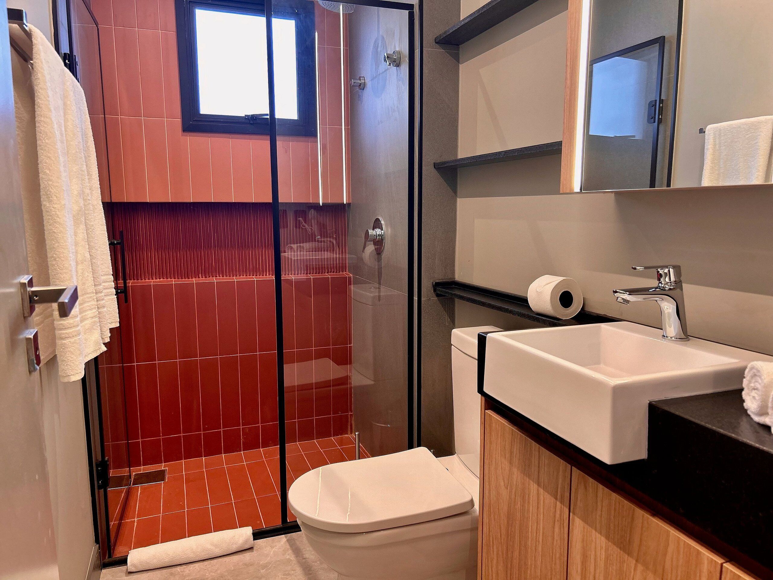 A bathroom with a glass shower enclosure, a toilet, a sink, and a mirror.