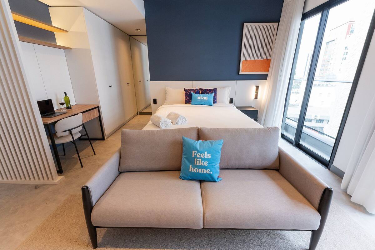 Ett modernt hotellrum med en säng, en soffa, ett skrivbord och ett stort fönster.