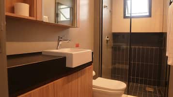 Un baño moderno con tocador de madera, lavamanos blanco y cabina de ducha con mampara de vidrio.