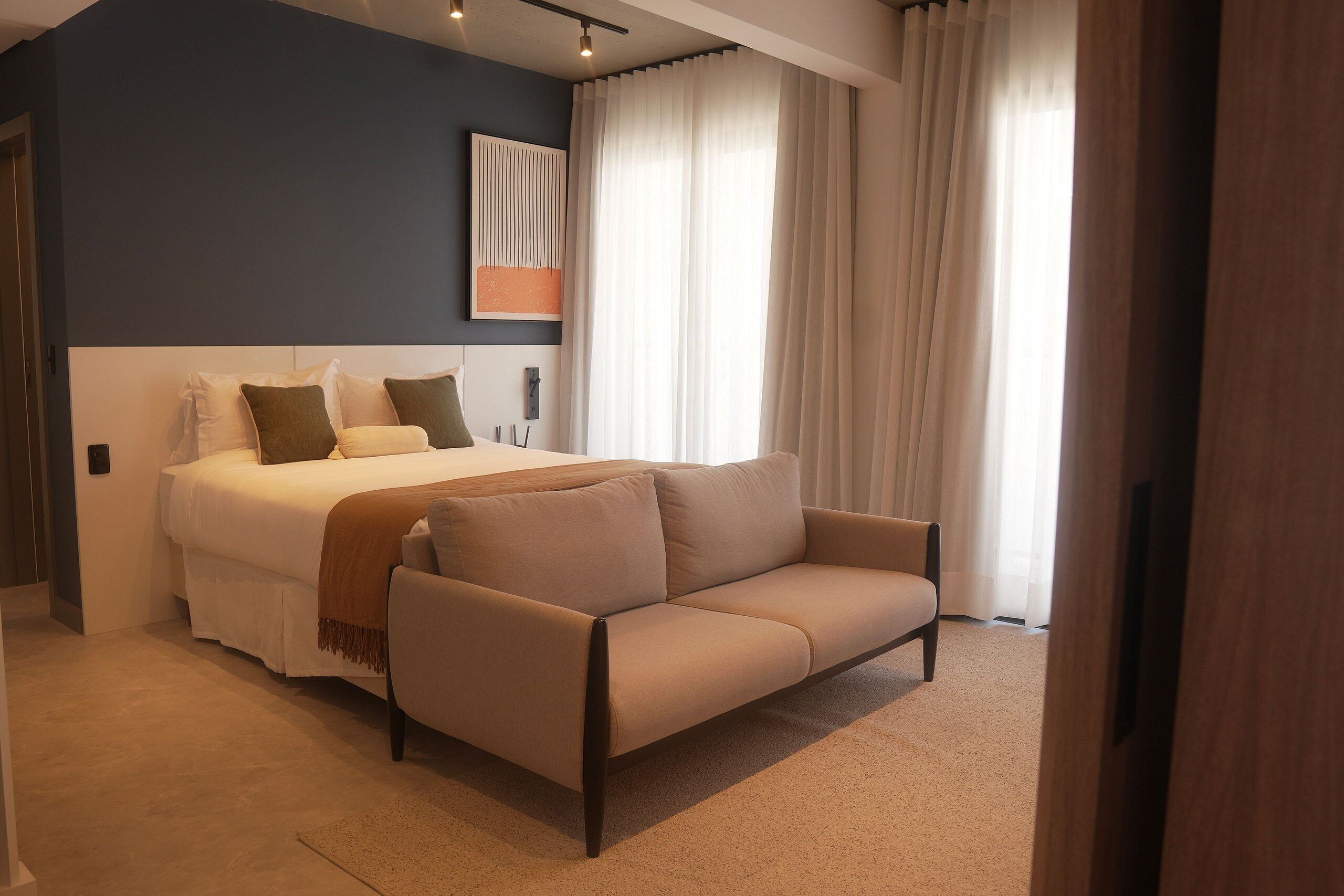 A modern bedroom with a large bed, a sofa, and a painting on the wall.
