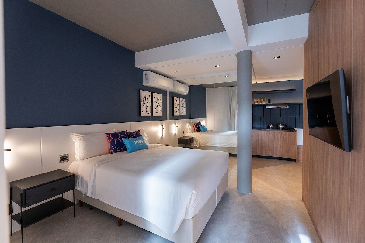 Ett modernt hotellrum med en stor säng, sängbord, en TV och en liten köksdel.