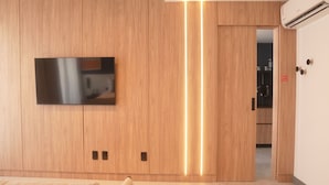 A modern room with a wooden wardrobe, a flat-screen TV mounted on the wall, and a hallway leading to a kitchen. - Xtay Oslo Florianópolis (Florianópolis)