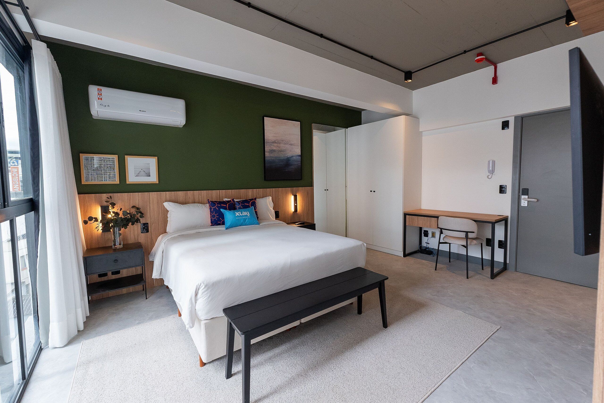 A modern bedroom with a large bed, bedside tables, a desk, and a bench.