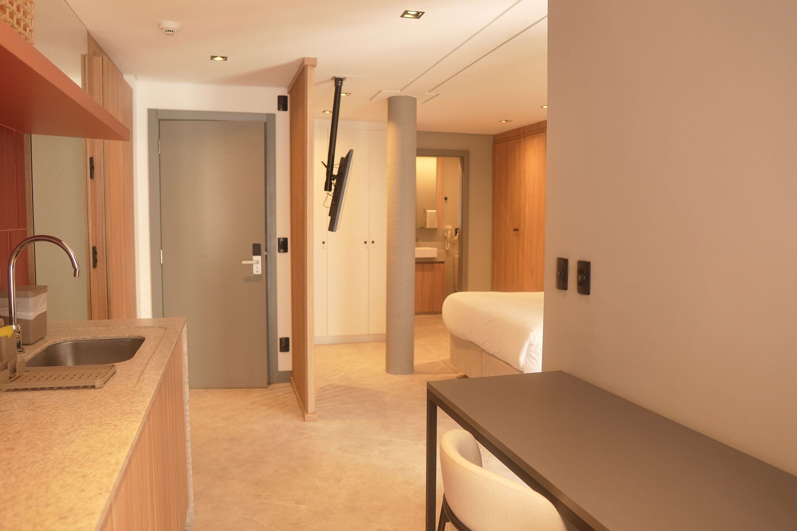 A modern hotel room with a kitchenette, a bed, and a sitting area.
