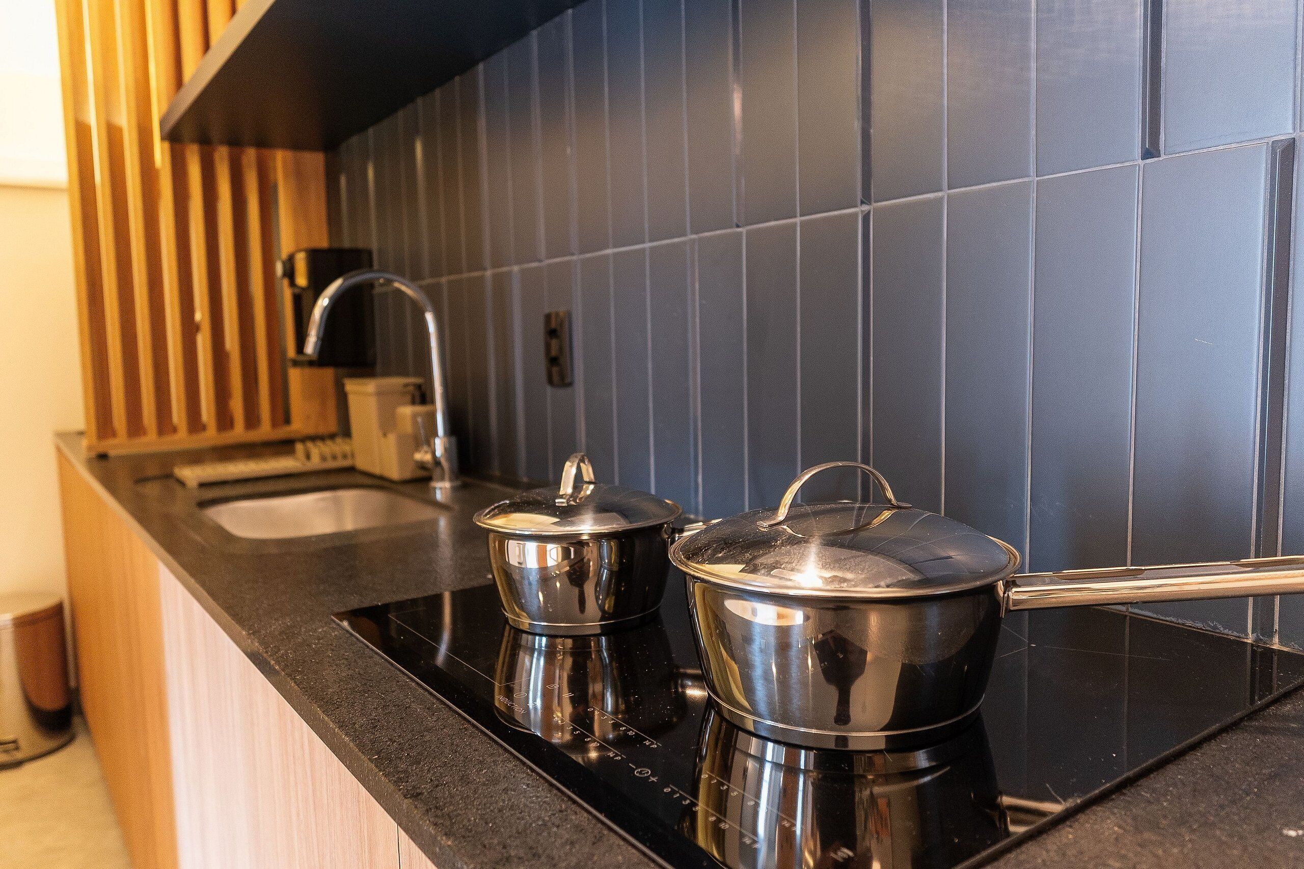 Una cocina con encimera negra, ollas de acero inoxidable, un lavabo y un armario de madera.