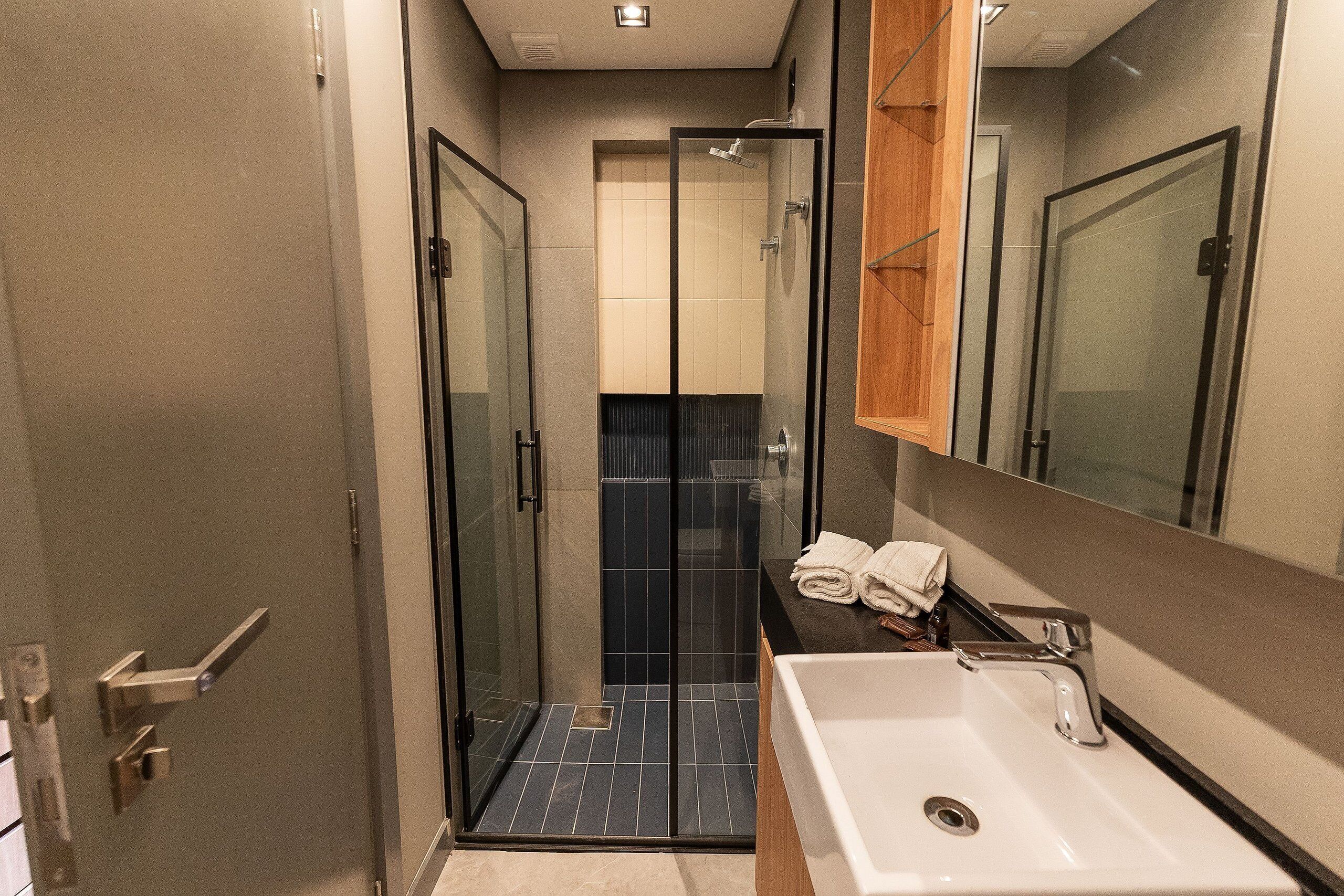 Une salle de bain moderne avec une douche à parois de verre, un lavabo blanc et un miroir au-dessus.
