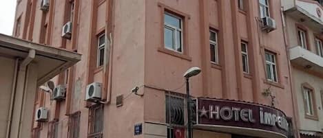 A pink building with multiple windows and air conditioning units. There is a sign for a hotel named "HOTEL IMPERIAL" and a sign indicating a parking area.