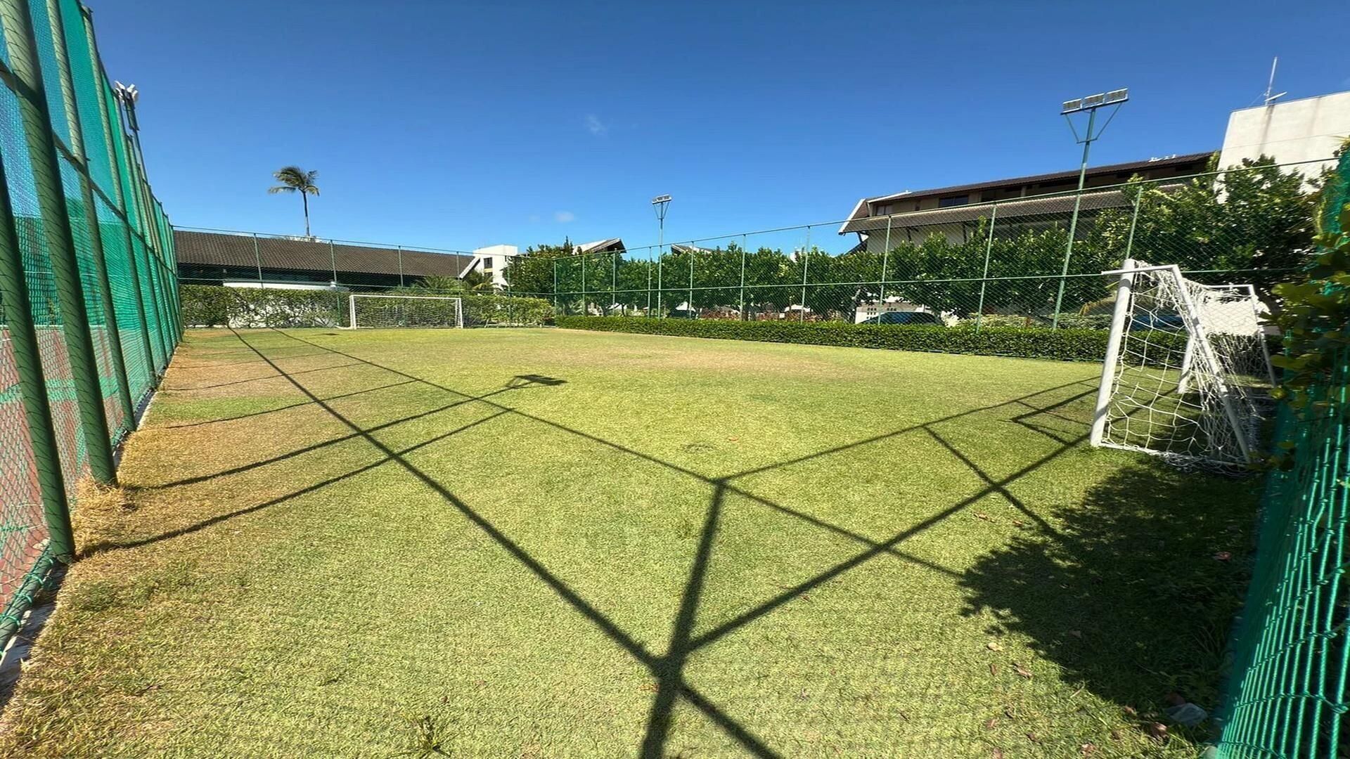 A soccer field with goalposts, surrounded by a green fence and trees.