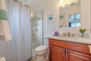 A bathroom with a glass shower enclosure, a toilet, a vanity with a sink, and a mirror.