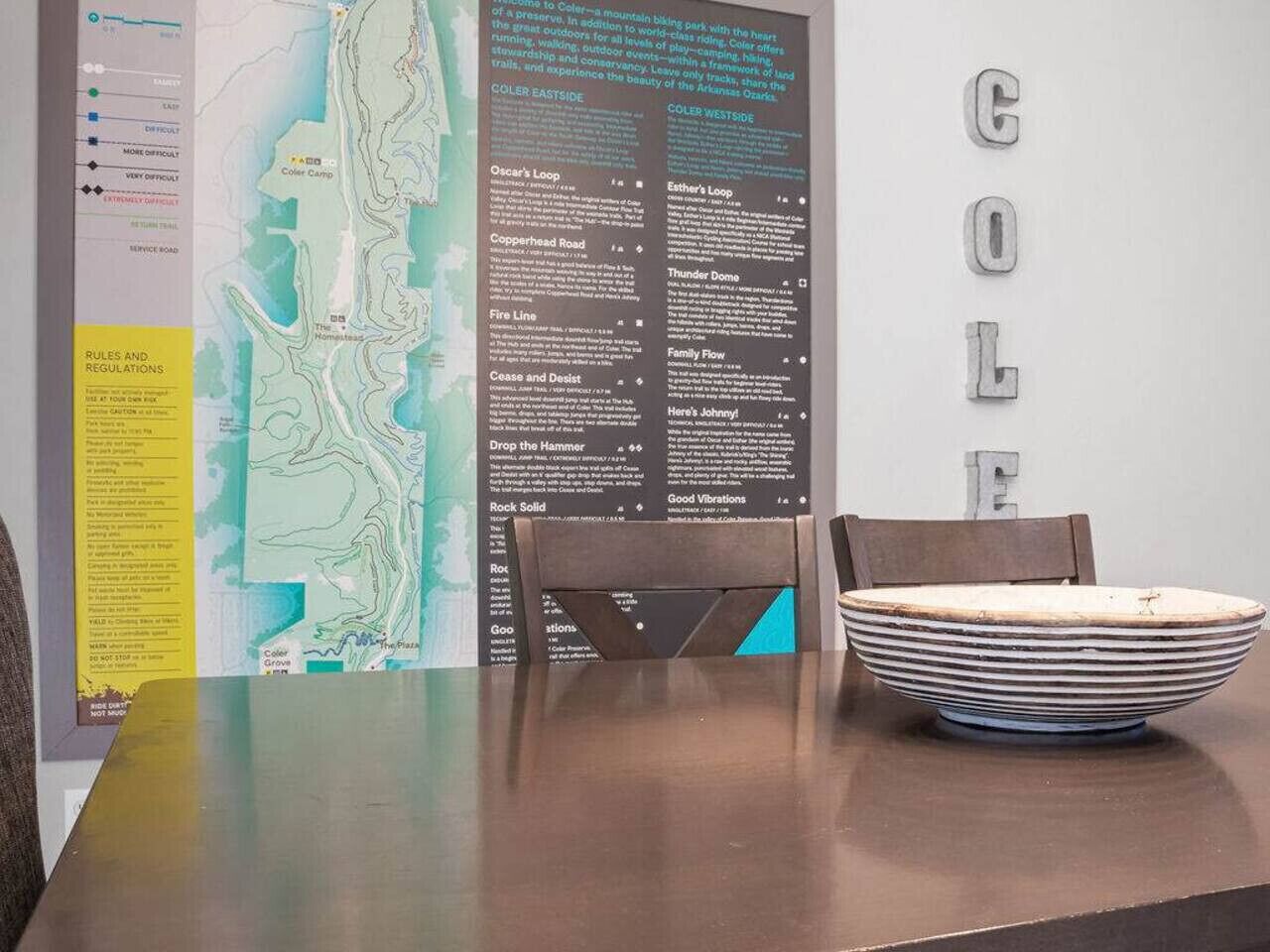 A dining table with a placemat, a bowl, and a chair. A map and informational poster are on the wall.