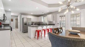 A modern kitchen with white cabinets, a central island with stools, and a dining table with chairs.