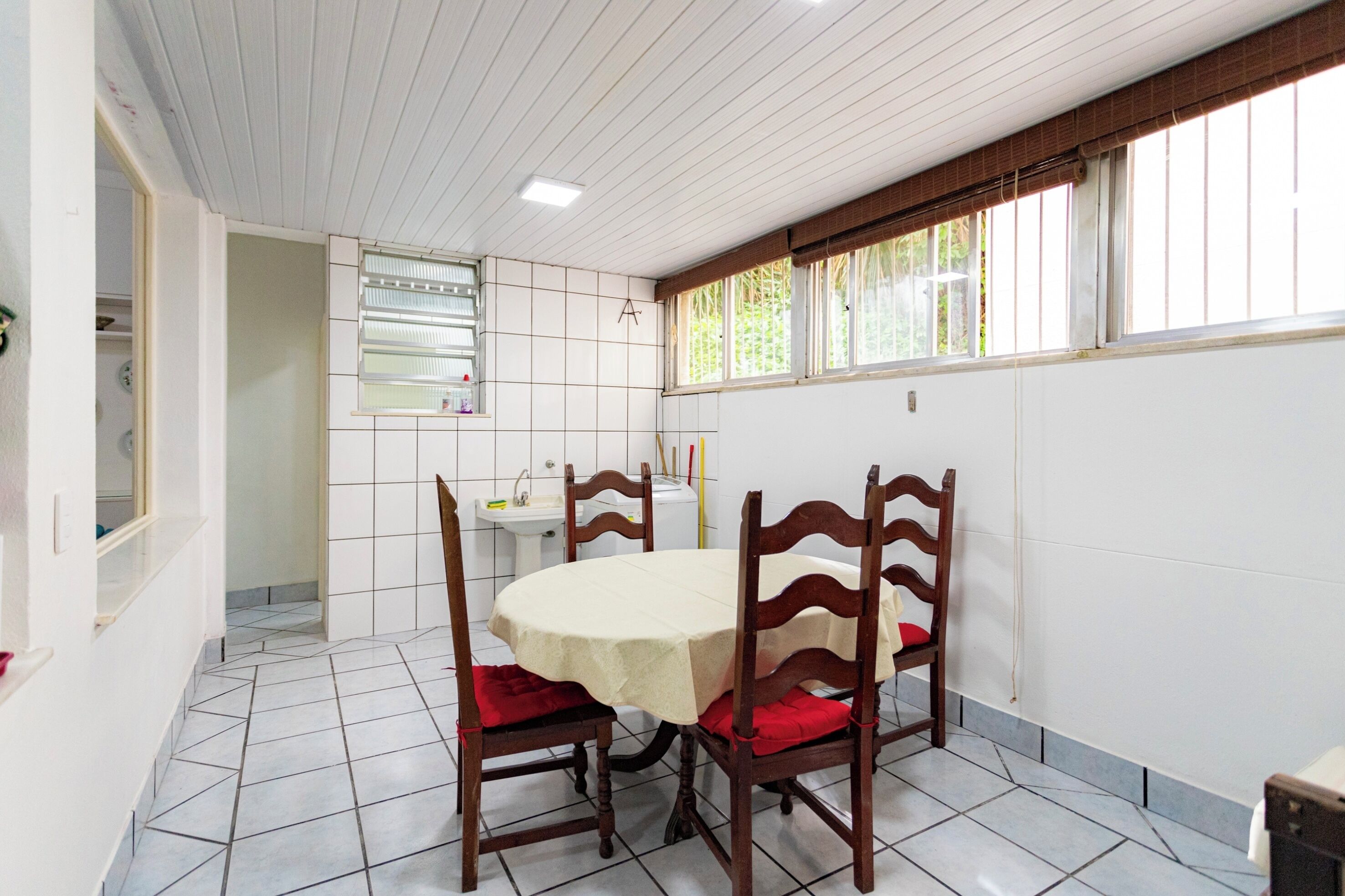 A dining area with a round table, four wooden chairs, a tiled floor, a window with blinds, and a white sink.