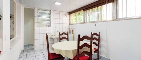 A dining area with a round table, four wooden chairs, a tiled floor, a window with blinds, and a white sink.