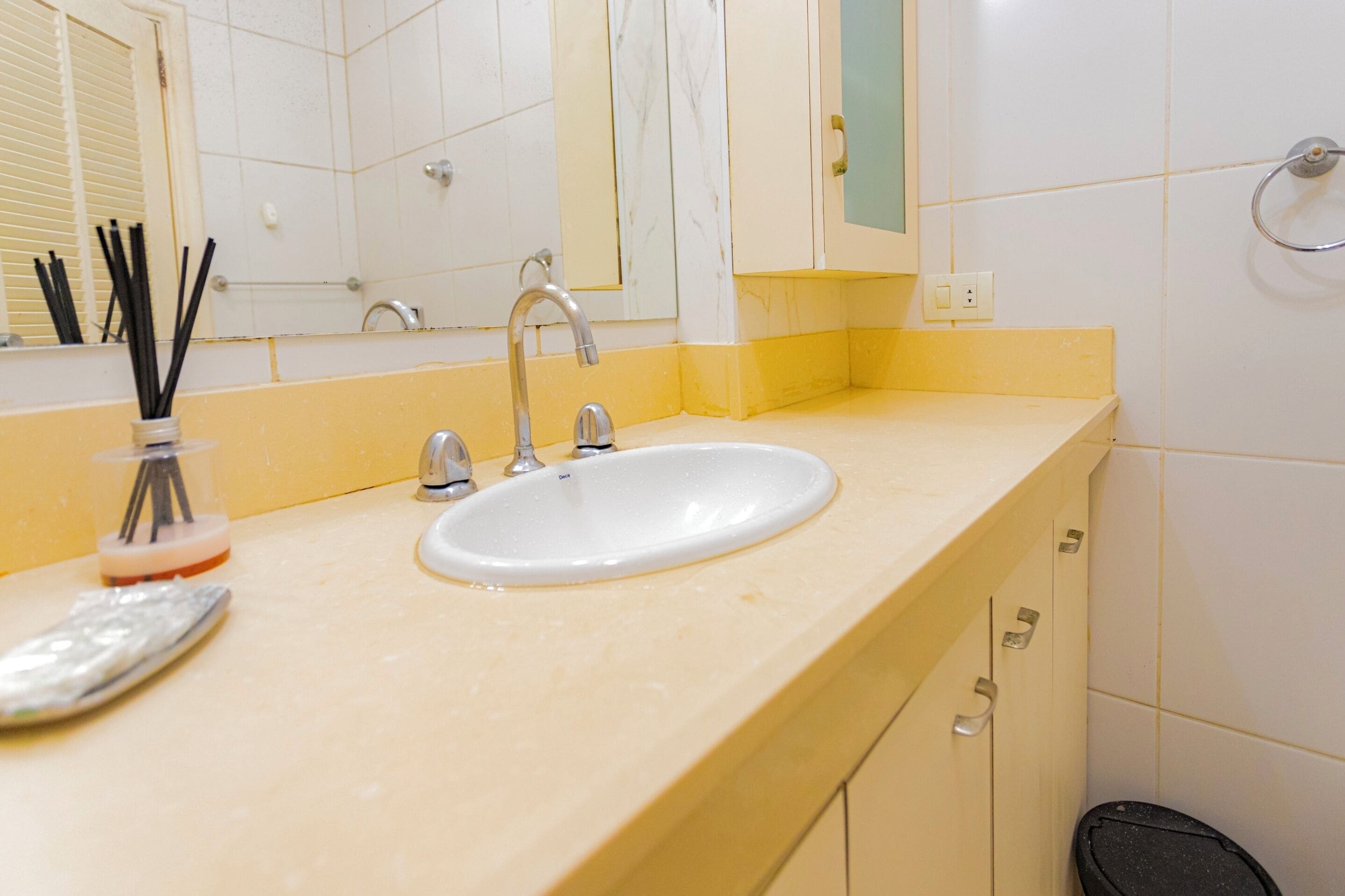 Un baño con lavamanos, espejo y un cubo de basura.