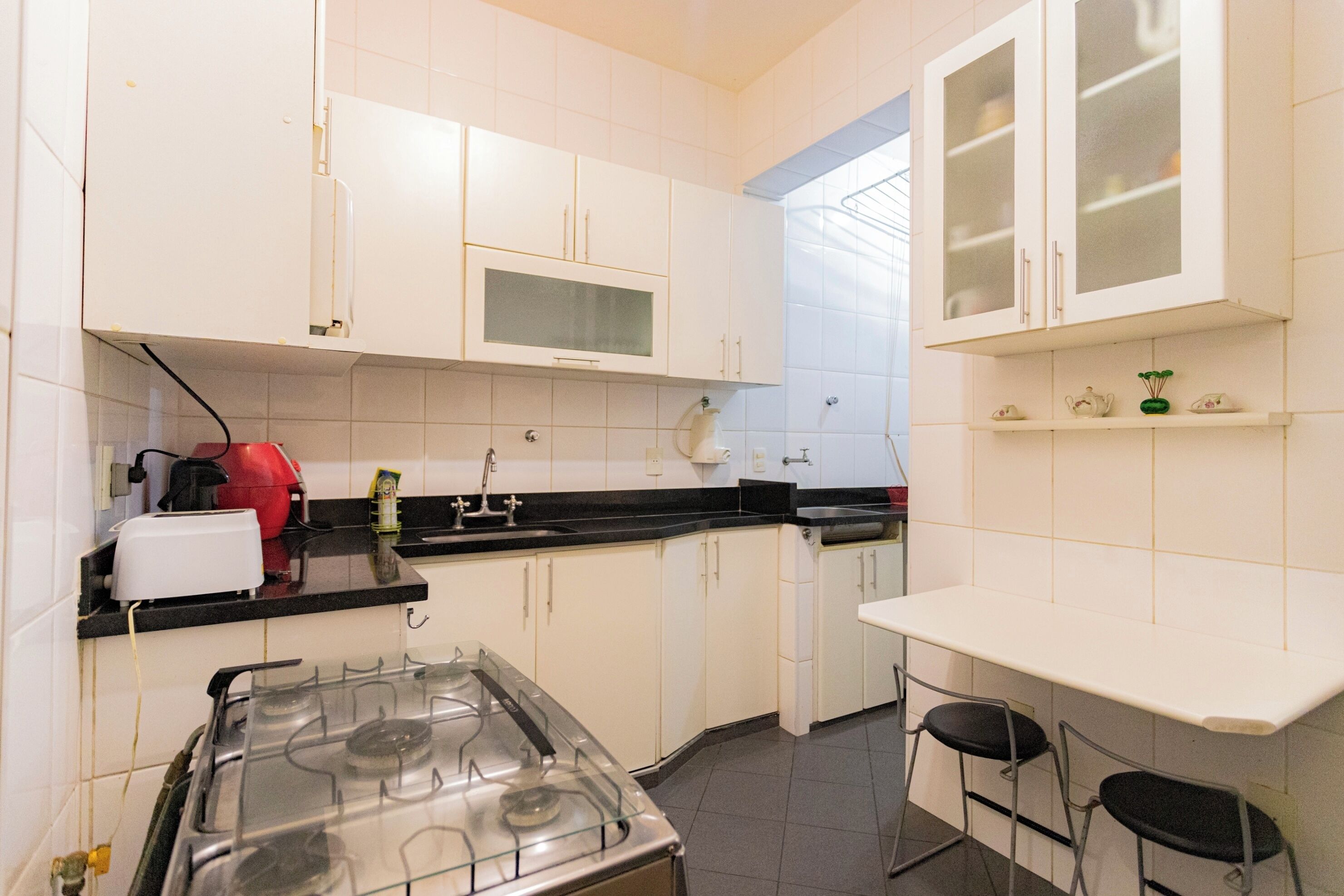 A kitchen with white cabinets, a gas stove, a microwave, and a sink. There are two chairs at a small table.