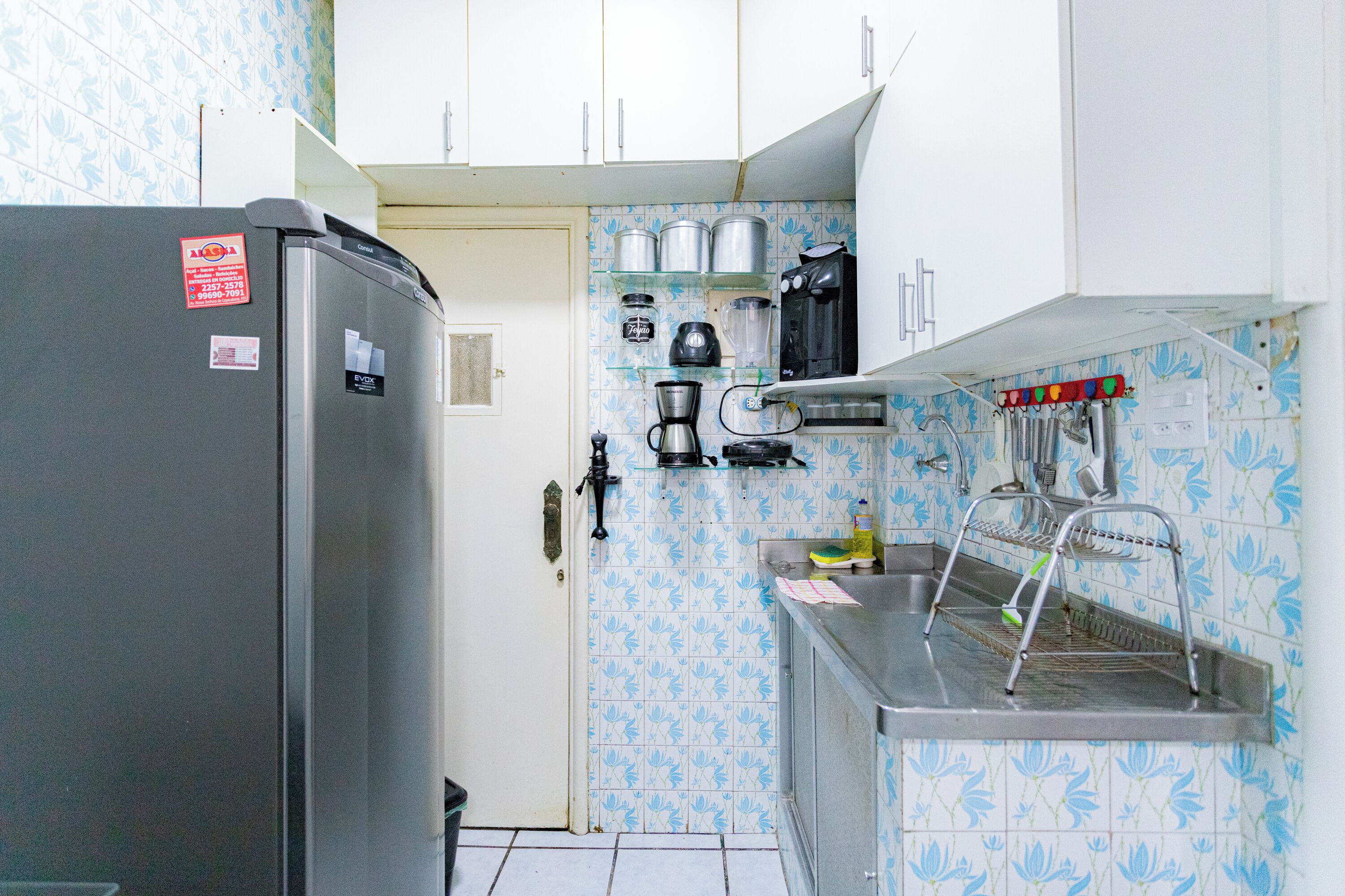 A compact kitchen with a refrigerator, coffee maker, and a sink with a drying rack.
