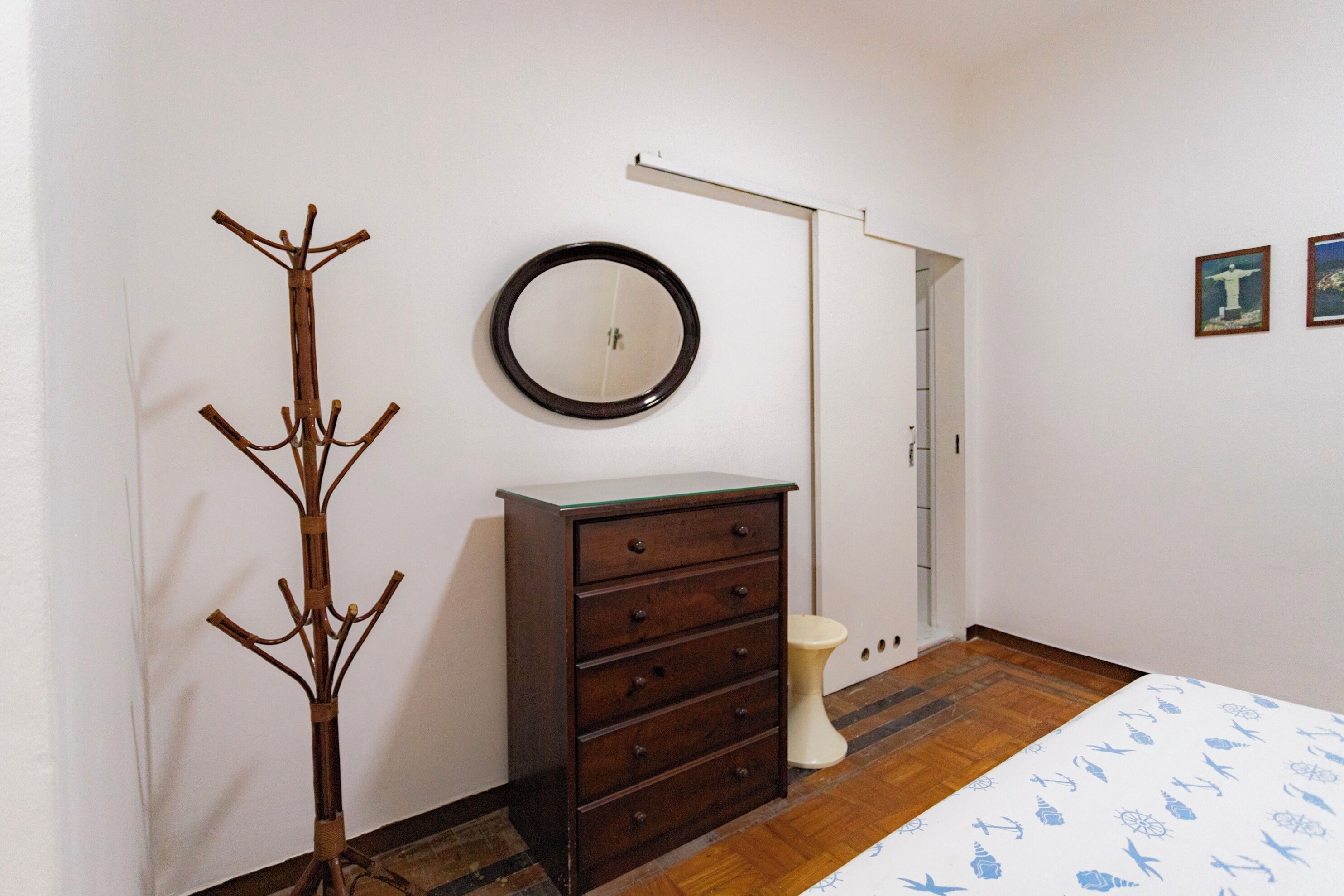 Een kamer met een houten kapstok, een dressoir met laden, een ronde spiegel en een bed met een gestreept beddegoed.