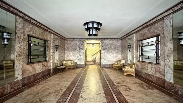 Een ruime lobby met marmeren vloer, een centraal hanglamp en gouden stoelen.